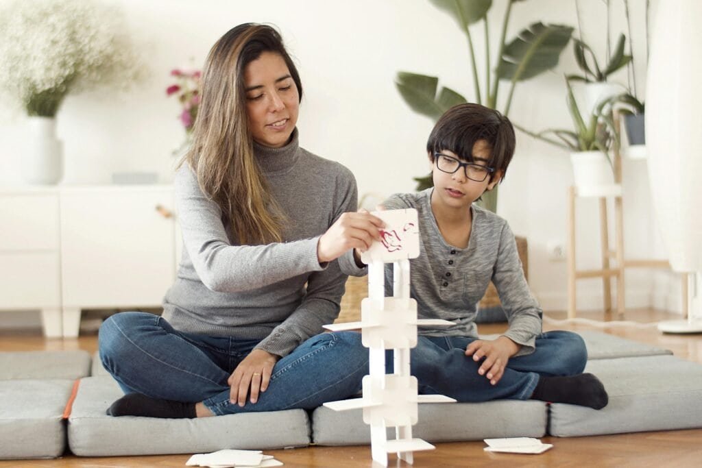Parenting in the Modern Era 3 Mother and son building a card tower together indoors, creating a joyful family moment.
